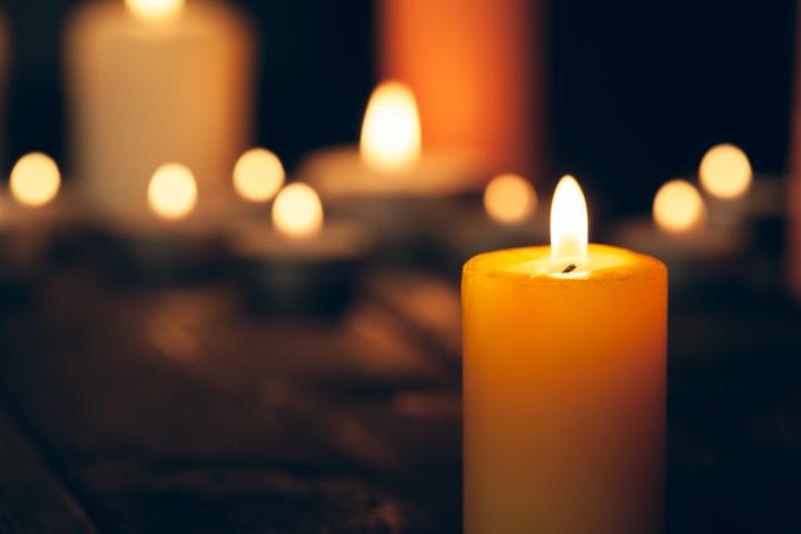 A burning candle in foreground with blurred burning candles behind it in on a black background