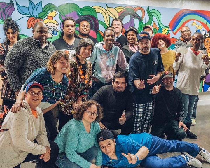 Large group of people pose in front of a colorful mural