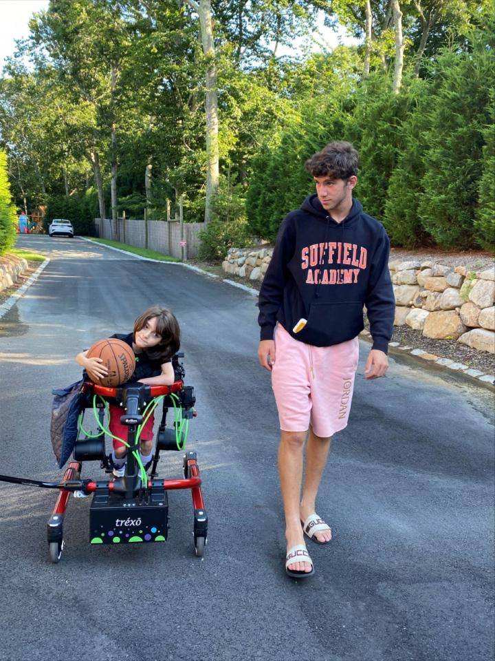Jackson holds a basketball while using the Trexo gait trainer, his brother walks alongside him