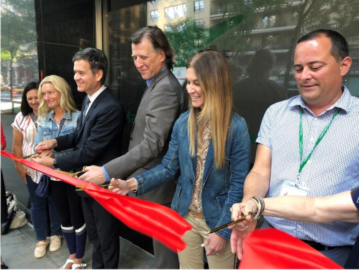 A group of people in a line, four of them have sissors and are cutting a red ribbon in front of them