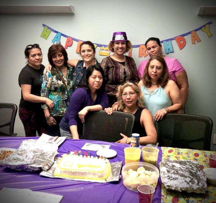 Group of people stand in front of bunting flags on wall and a table with food and a purple table cloth