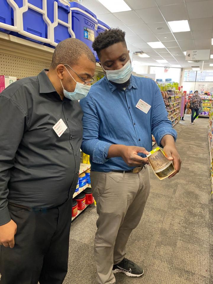 Portrait of Shakar Hollins (left) with a colleague (right) at CVS they are wearing disposable face masks and looking at an item