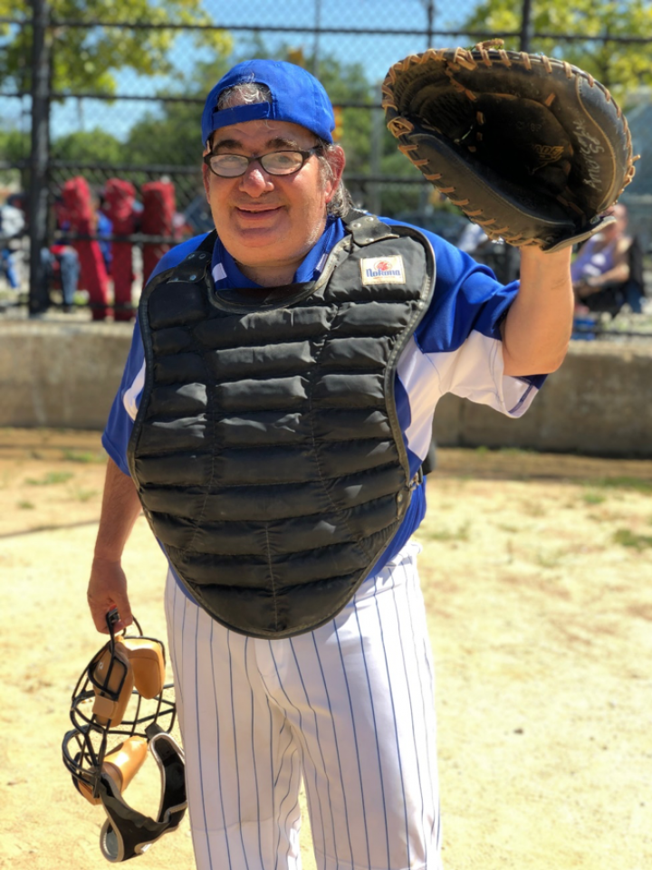 Man stand wearing a baseball uniform and has his left hand up wearing a baseball glove