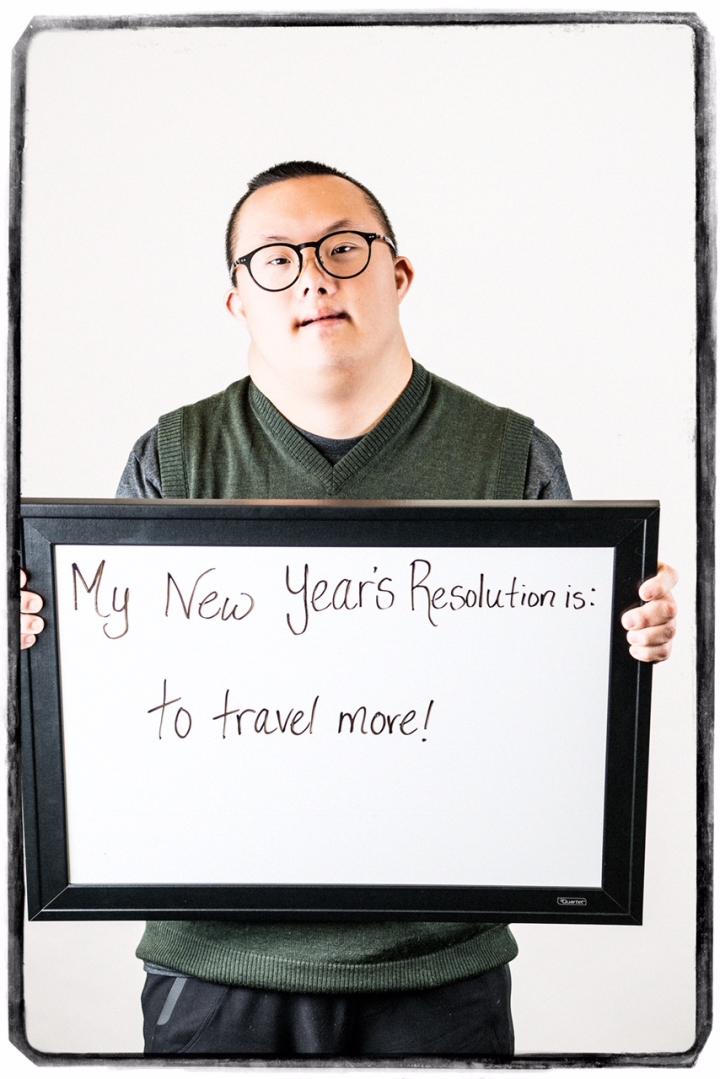 Photograph of man holding sign "My New Year's Resolution is: to travel more!"