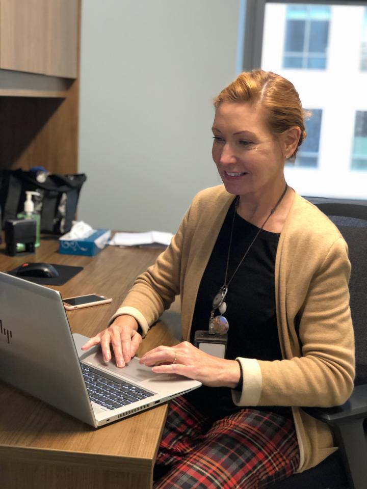 Woman sits at a desk with a laptop open in front of her