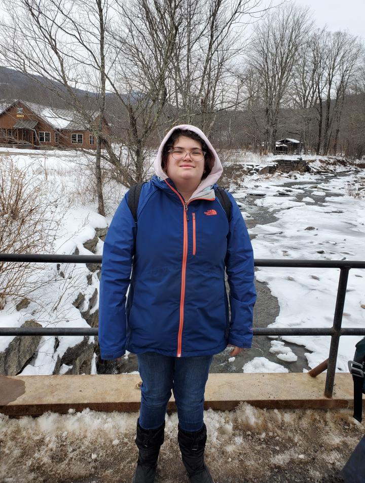 Ashley wearing a dark blue coat is outside with snow in the background landscape. 