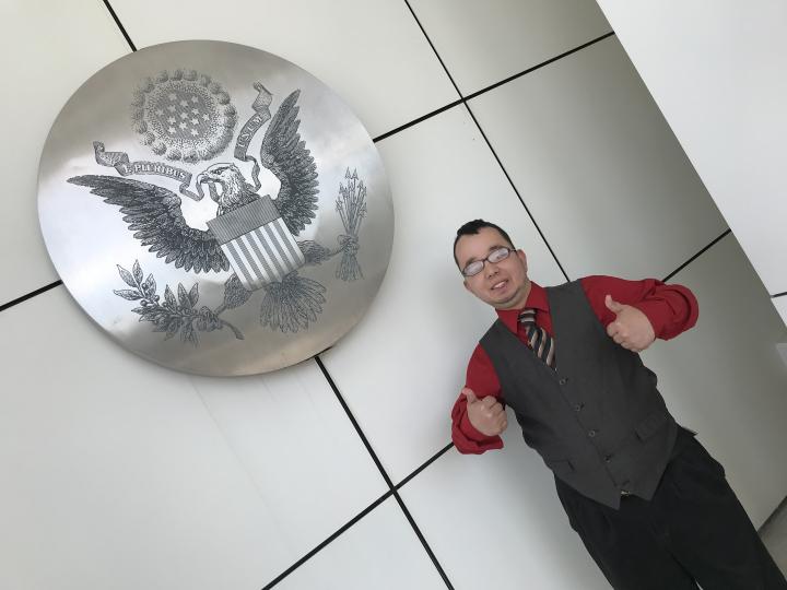 Alex stands by an etched picture of an American Eagle on a large silver colored disc