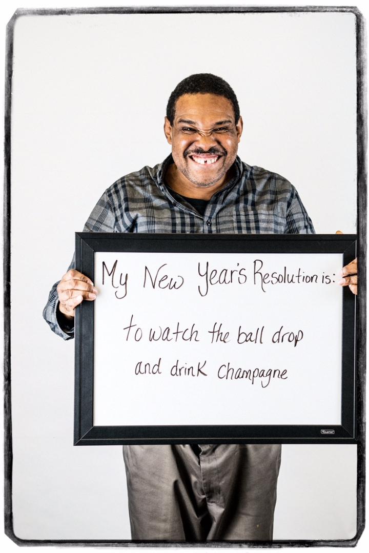 Photograph of man holding sign "My New Year's Resolution is: to watch the ball drop and drink champagne"
