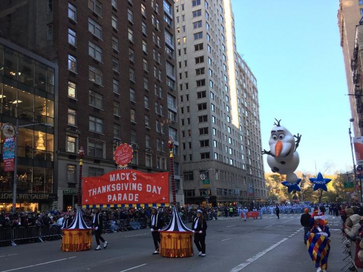 Photograph of the beginning of the Macy's Thanksgiving Day Parade with people marching with the parade sign and Olaf the snowman