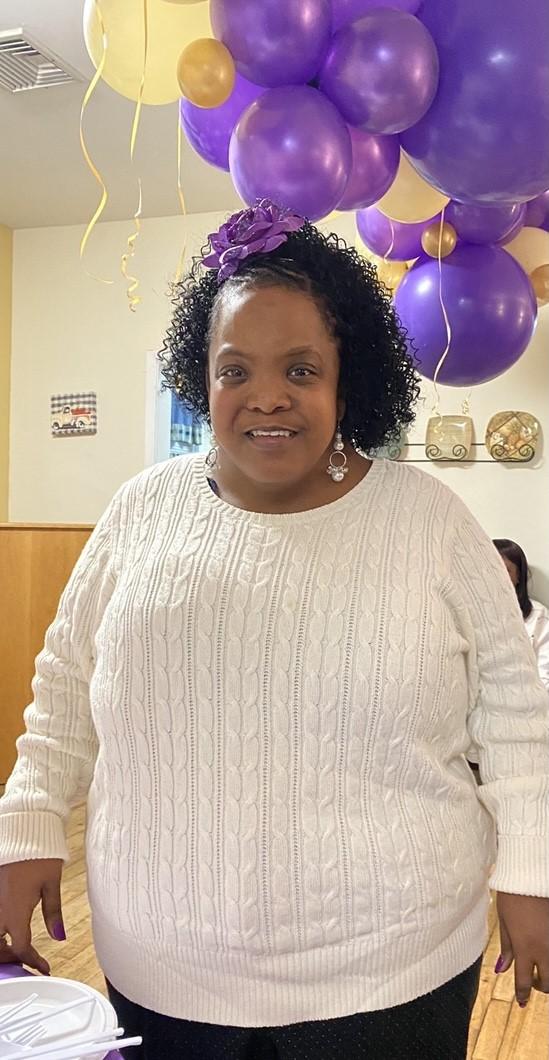 Latasha stands in a room with many purple balloons behind her, she is smiling for the photo