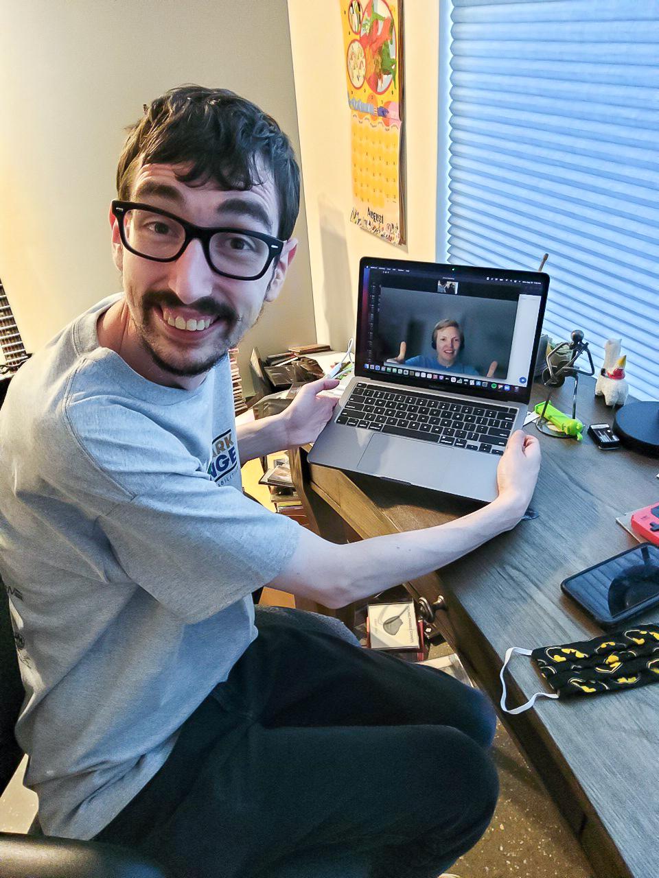 Matthew sits at a desk holding a laptop. You see the screen has a zoom call with Carol on the video