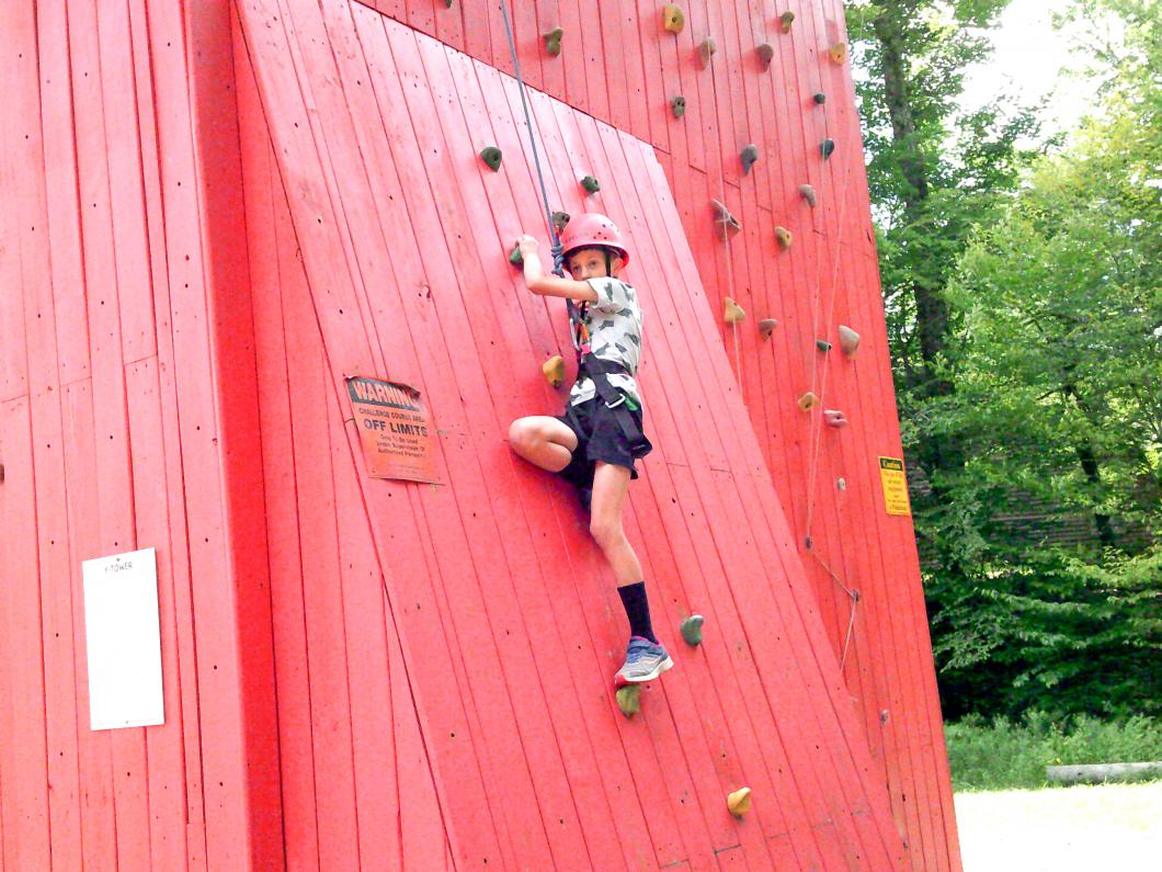 Child wearing rock climbing harness appears to be ascending on a red climbing wall.