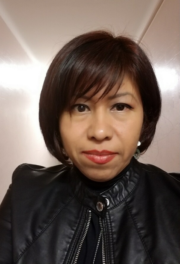 Selfie of Laura mendoza, she wears a black jacket, hair cut into a bob and looks to be standing in a white painted hallway.