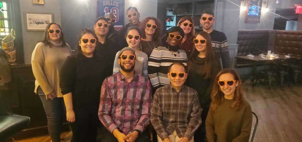 Group of people sitting and standing together posing for picture, all wearing the same glasses