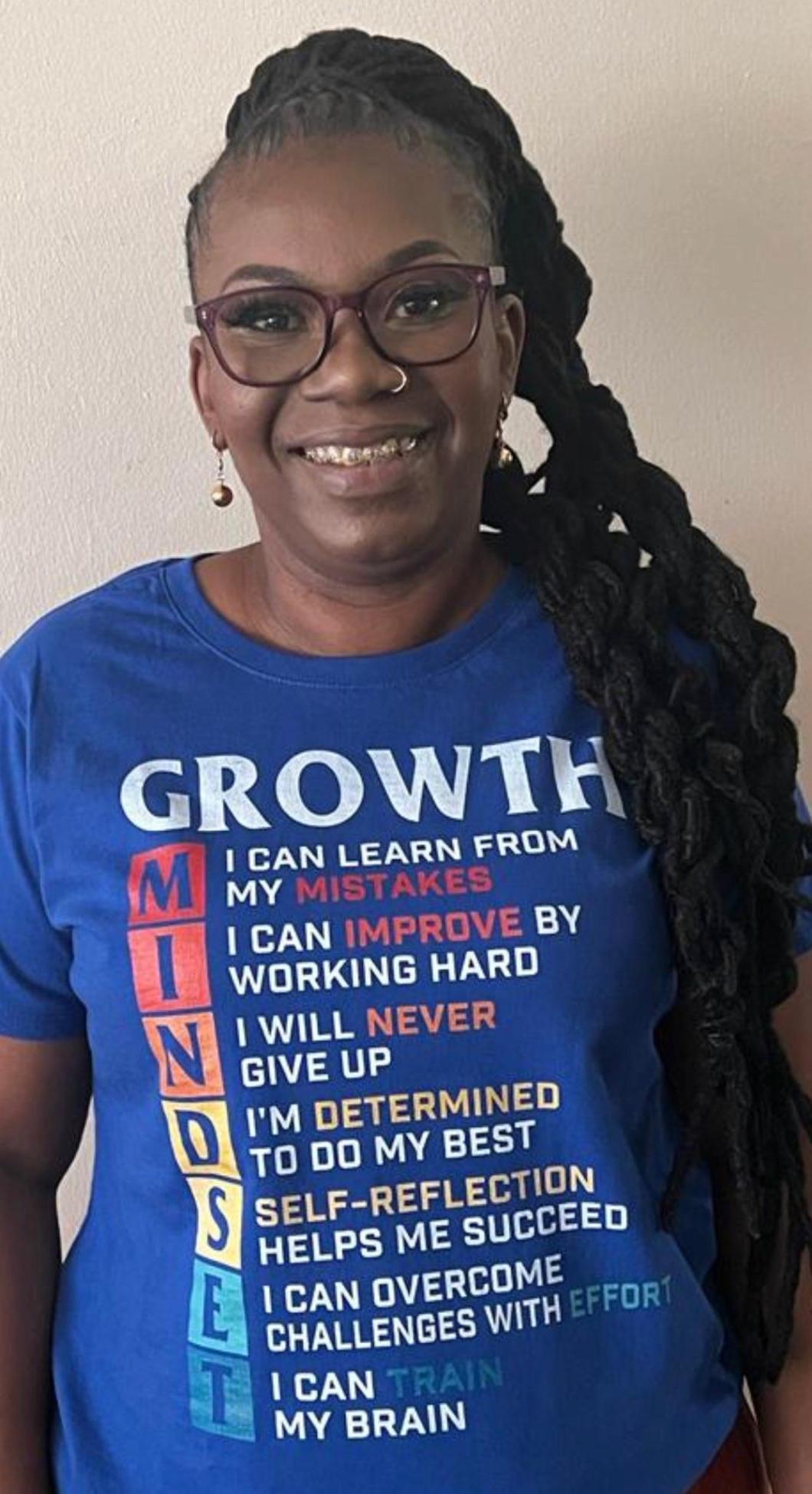 Person with a long hair braided to one side wears glasses and a blue shirt that says "Growth" and then sentences about Mindset