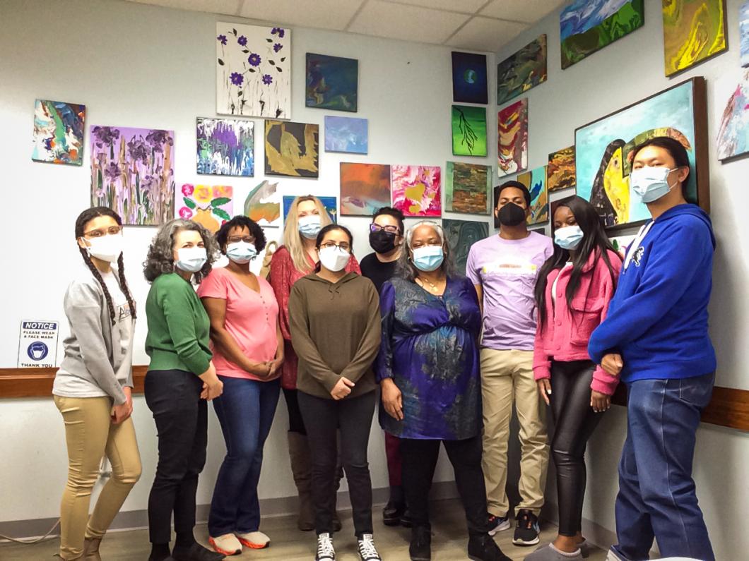 Group of 8 people wearing masks stand in front of 2 walls of artwork.