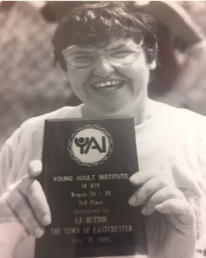 Black and white shot of someone with a big smile holding up a plaque with old YAI logo - from 1986