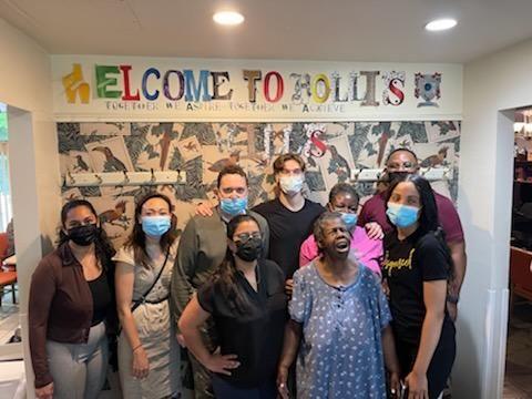 group of people pose for photo in front of a large sign that says "welcome to Hollis"