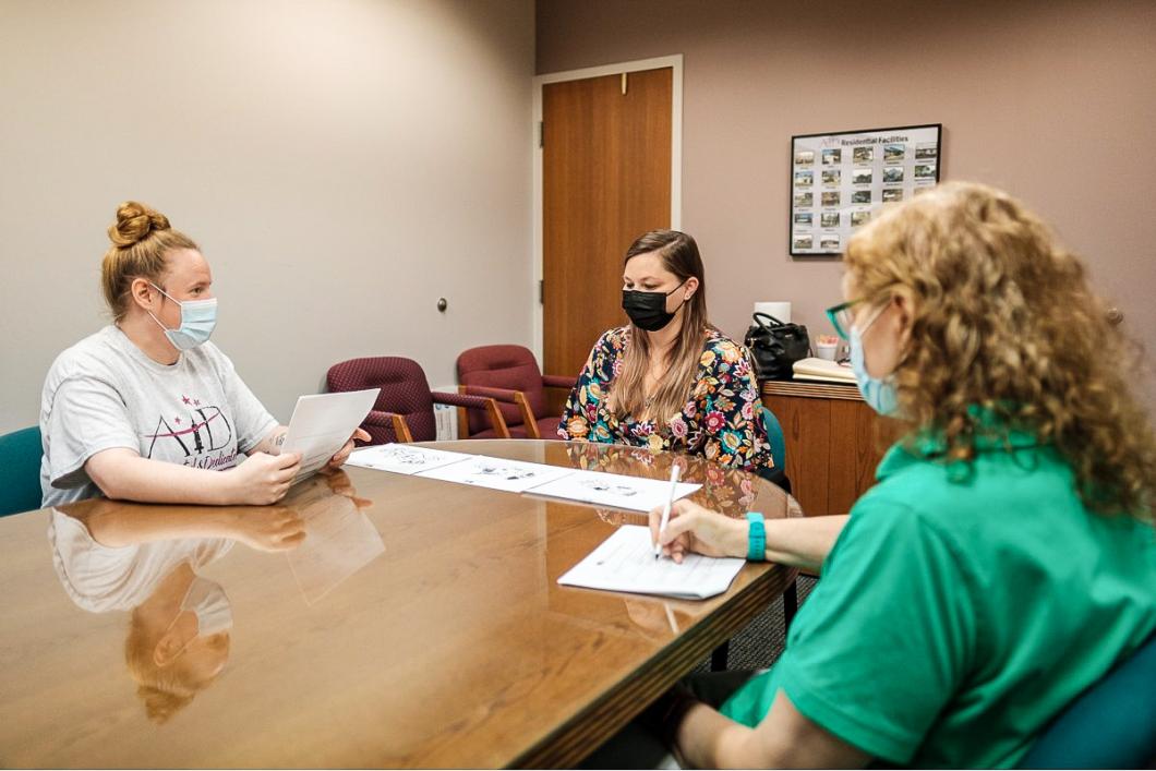 3 people sit at a table with illustrations placed on the table