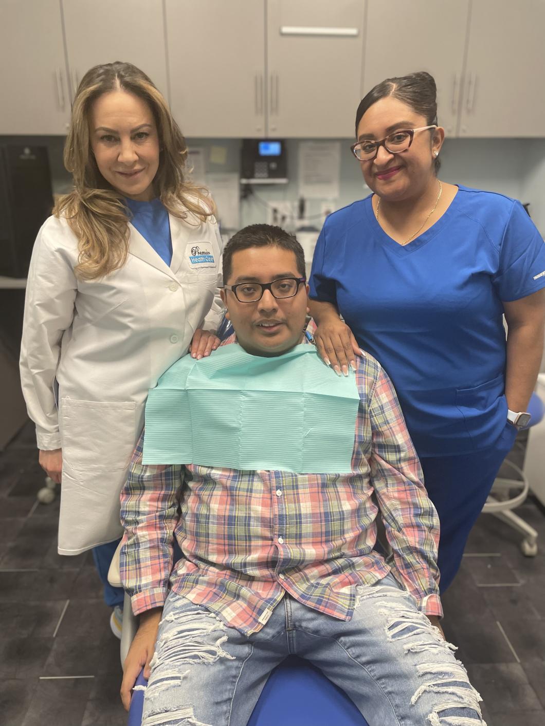 Kelvin poses in the dental chair with the dentist and clinician standing behind him on either side.