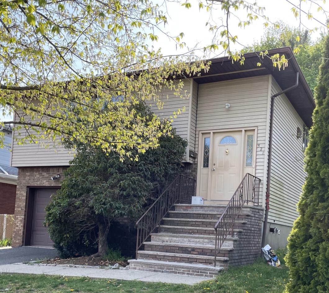 House with stairs to entrance, there are trees and bushes around it.