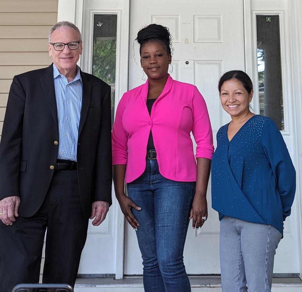 Three people stand outside front door to pose for photo