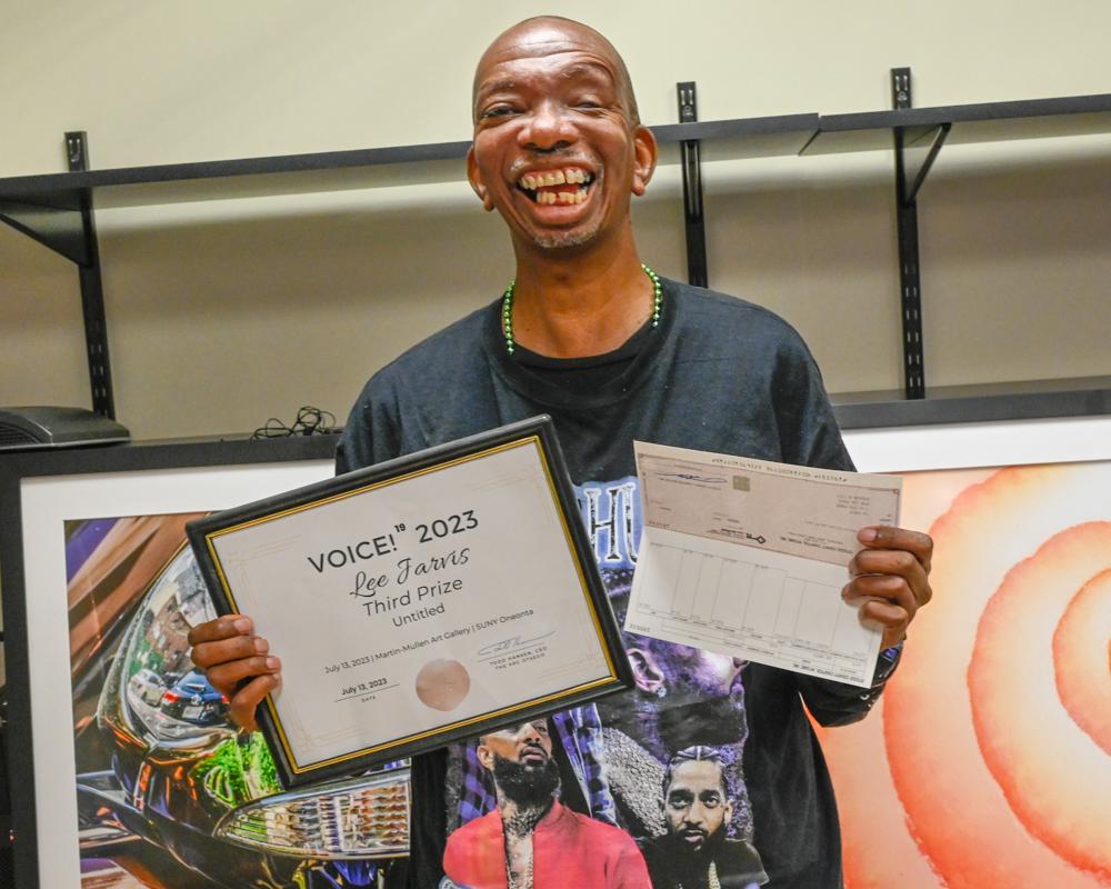 Lee stands with certificate and check award in his hands. He has a big smile on his face