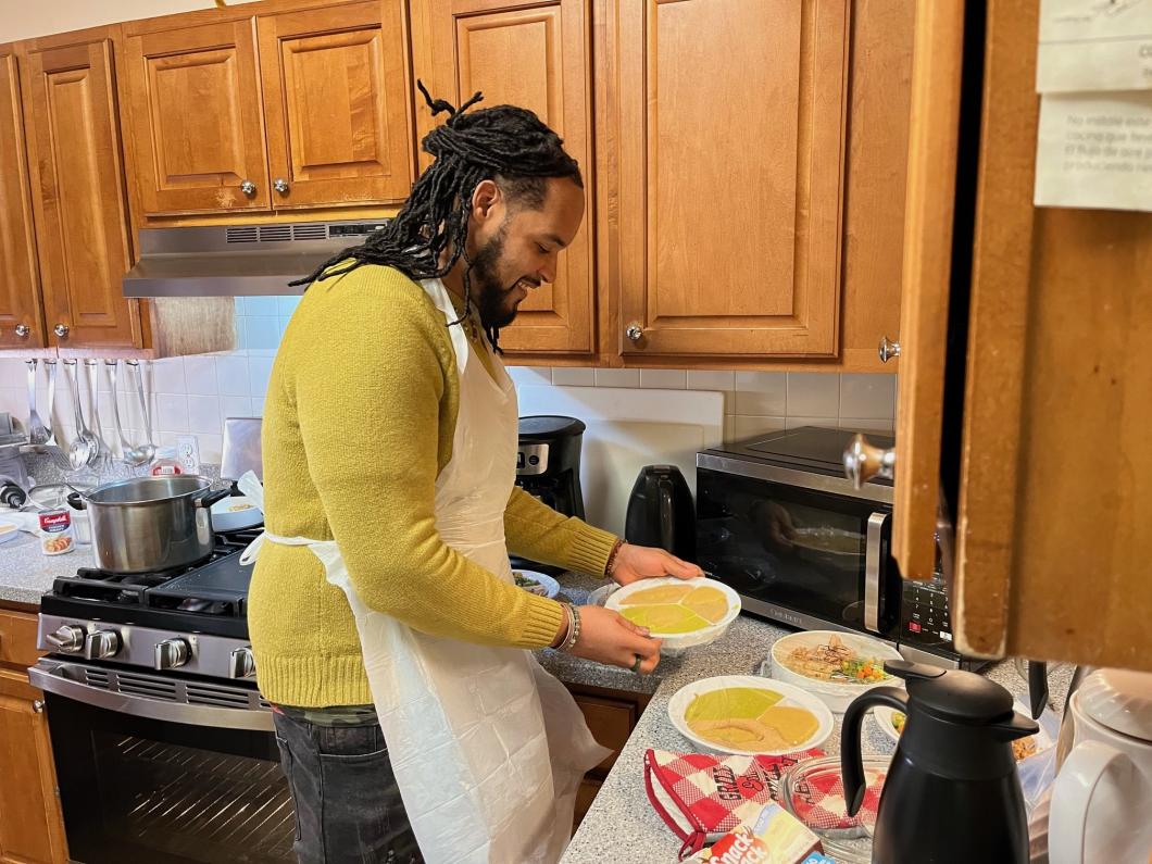Paez in a kitchen with apron on, he is holding a bowl of food