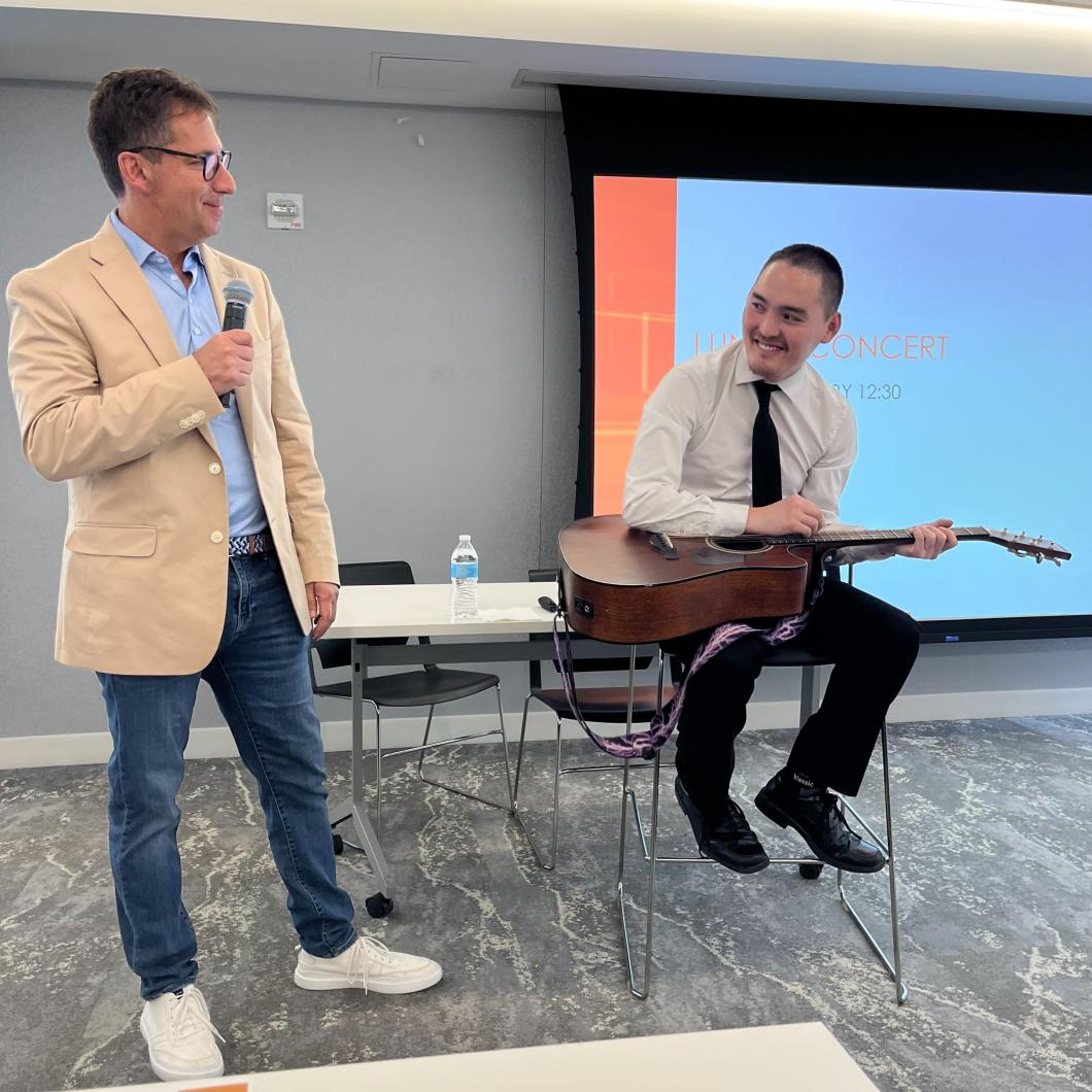 Gary stands on left holding a mic, while Ian sites on a high stool with a guitar in his lap.