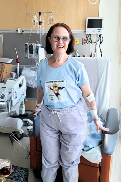 Janice stands and smiles in a hospital room, post-brain surgery.