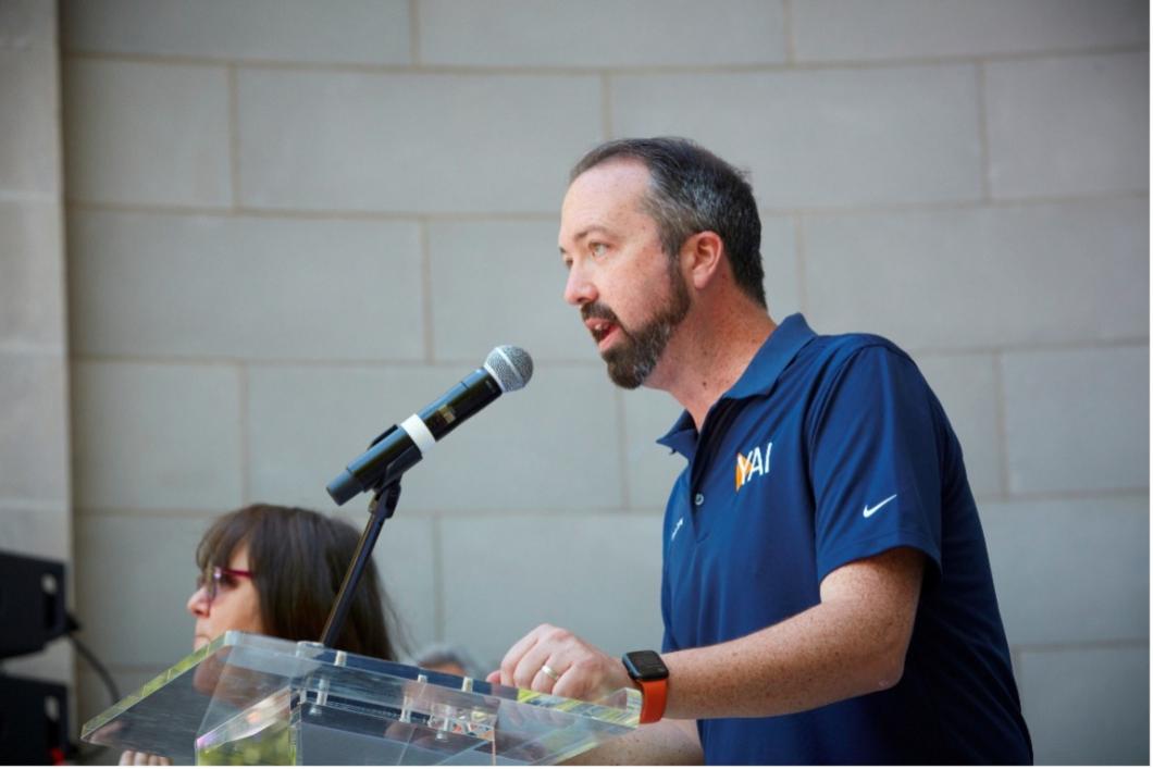 Kevin stands a podium at the bandshell in Central Park as he speaks to the audience at CPC