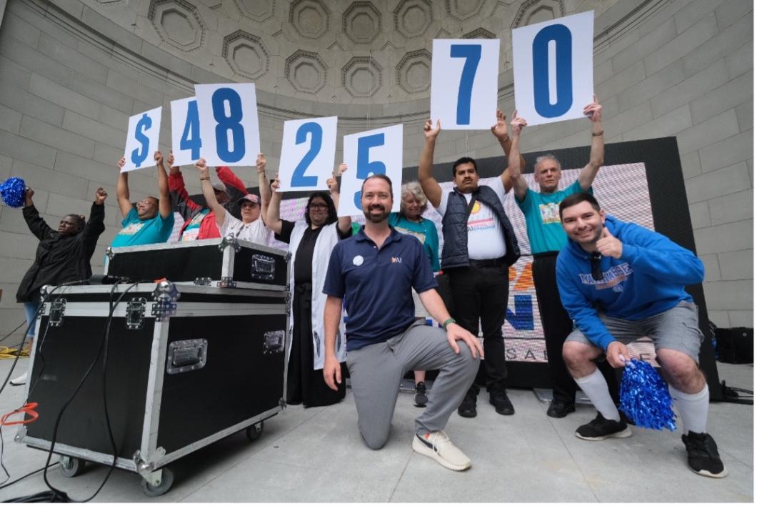 Kevin Carey kneels on the stage at the Central Park Challenge. He's surrounded by people connected to YAI