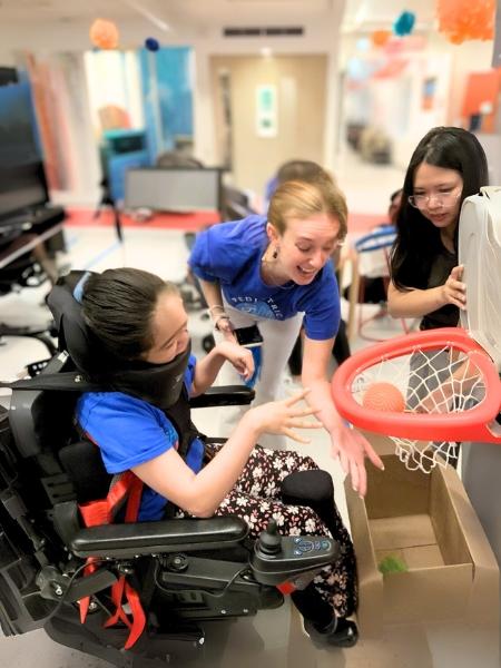 An iHOPE student plays adaptive basketball with support from staff