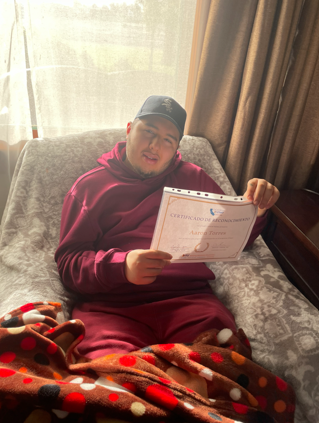 Aaron sitting on a couch holding a certificate.
