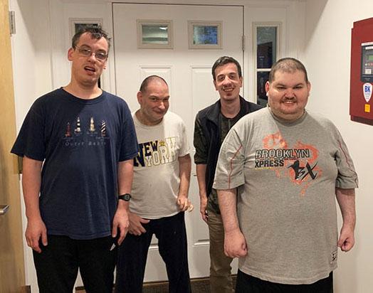 Four men stand inside by a door and pose for picture